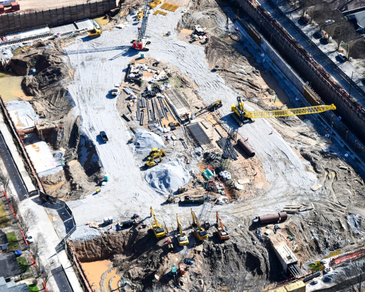 Aerial view: busy construction site with cranes, machinery, and nearby homes.