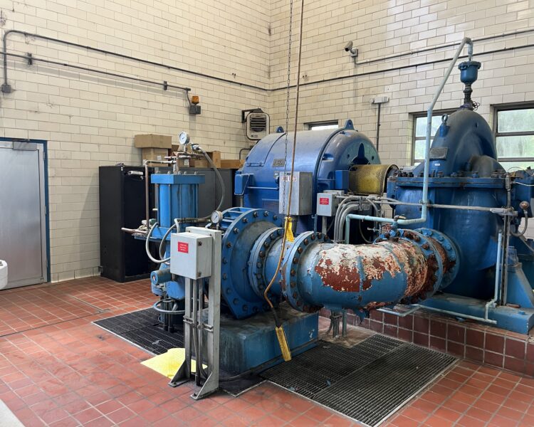 Large blue water pump and pipes on red tile in utility room.