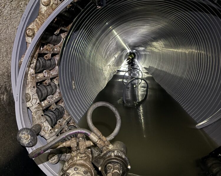 Corrugated metal pipe with water, cables, and machinery inside.