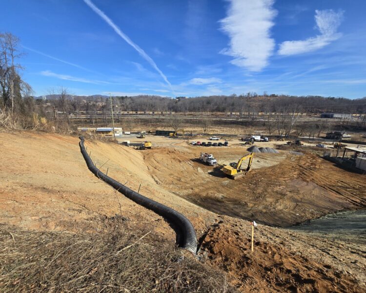 Excavators, trucks, and a large pipe on a dirt construction site.