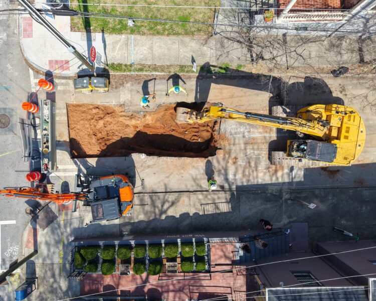 Vista aérea: obras en una calle de la ciudad con excavadoras y obreros.
