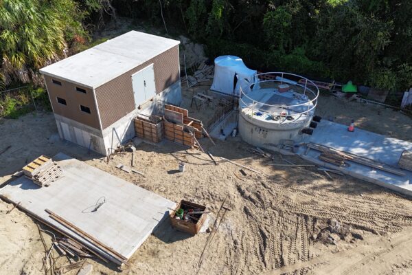 Vista aérea: edificio rectangular, estructura circular, materiales sobre arena.