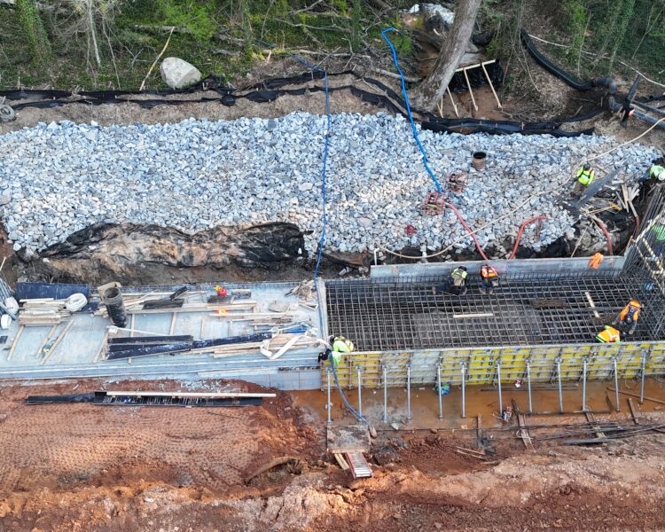 Obreros construyendo una estructura de hormigón en una obra situada cerca de unas rocas y un bosque.
