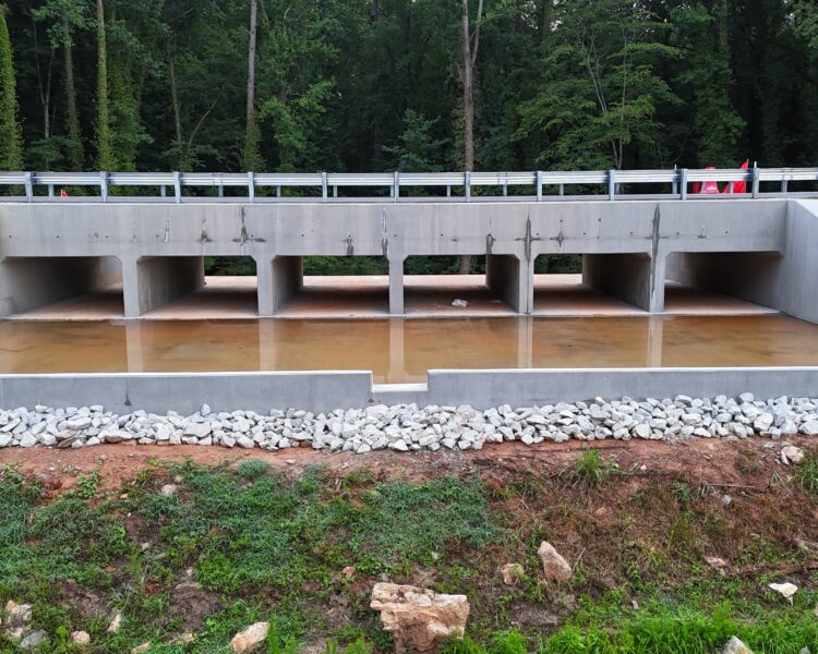 Alcantarilla de hormigón con cuatro aberturas bajo la carretera, rocas y árboles.