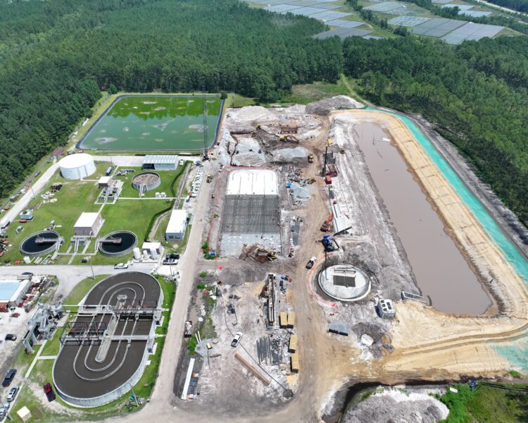Aerial shot of a wastewater plant, tanks, buildings, and nearby construction.
