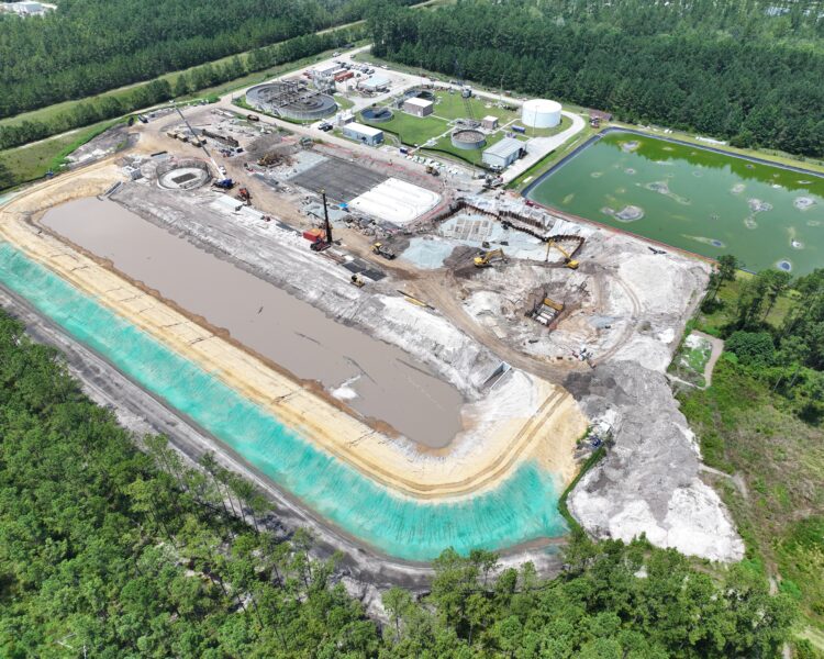 Aerial shot of construction site, excavators, sediment basin, forest.