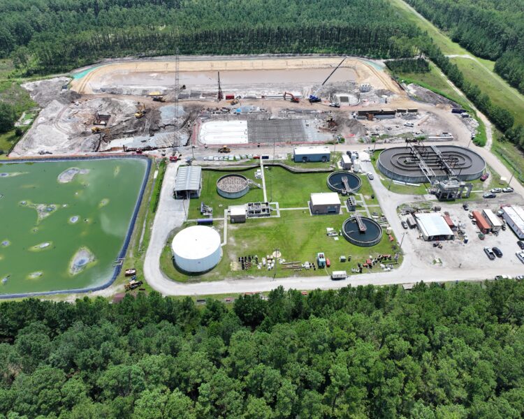 Aerial view: wastewater treatment plant, tanks, forest, pond.