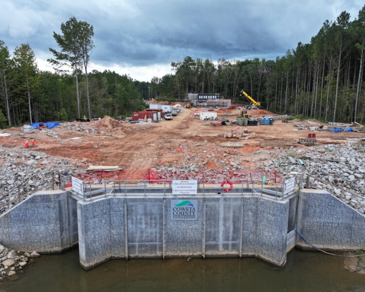 Construction site by woods, machinery, barrier sign, water nearby.