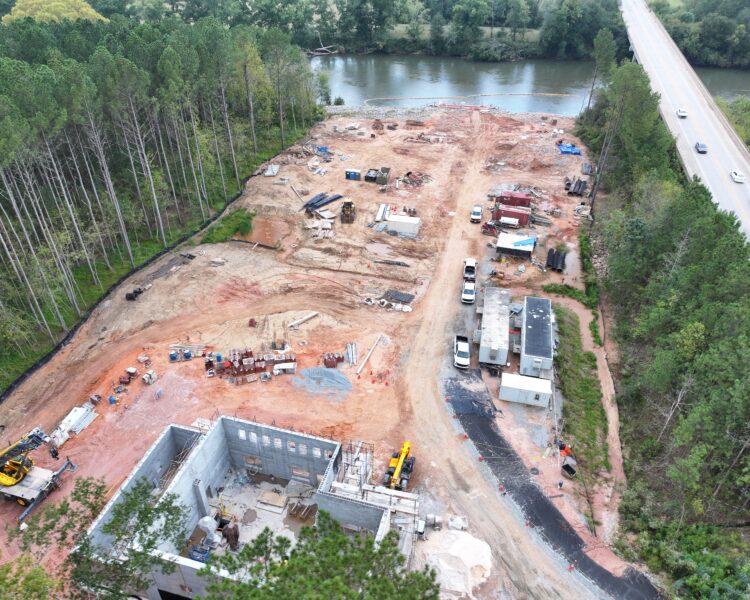 Aerial shot of riverside construction site with vehicles and trees.