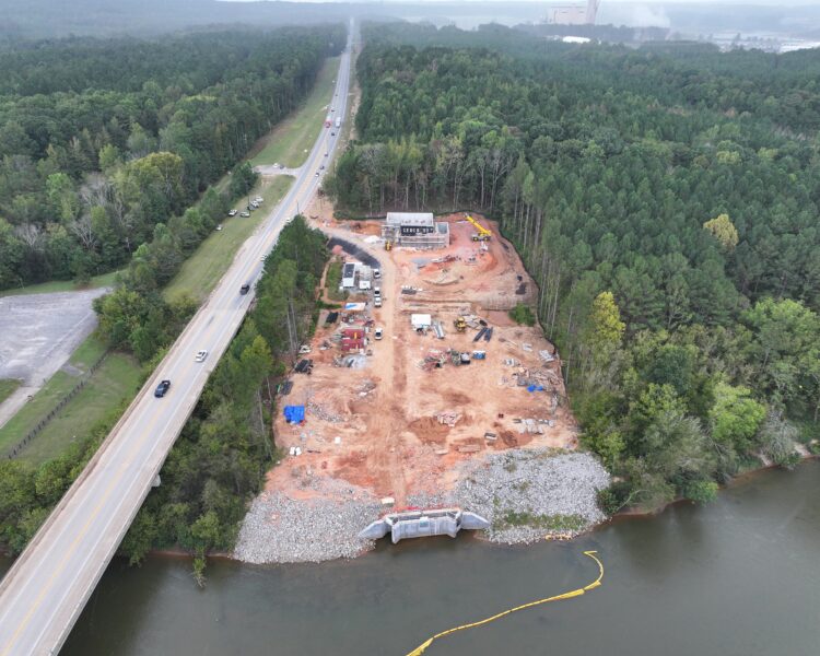 Construction site by river and forest, next to busy road.