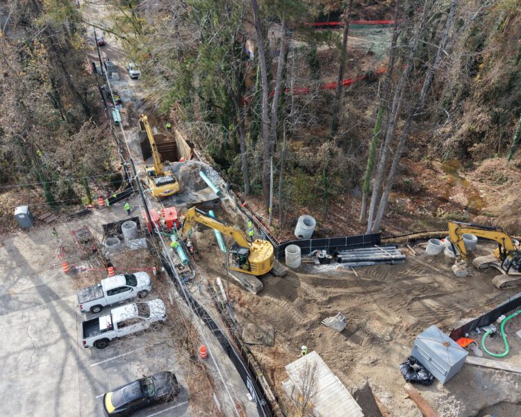Aerial view: construction site beside woods with vehicles and workers.