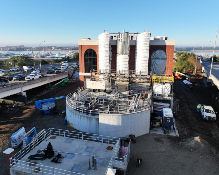 Construction site with tanks, scaffolding, brick building, nearby traffic.