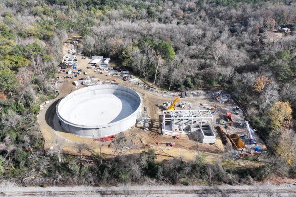Vista aérea: estructura circular, cimientos, árboles, maquinaria de construcción.