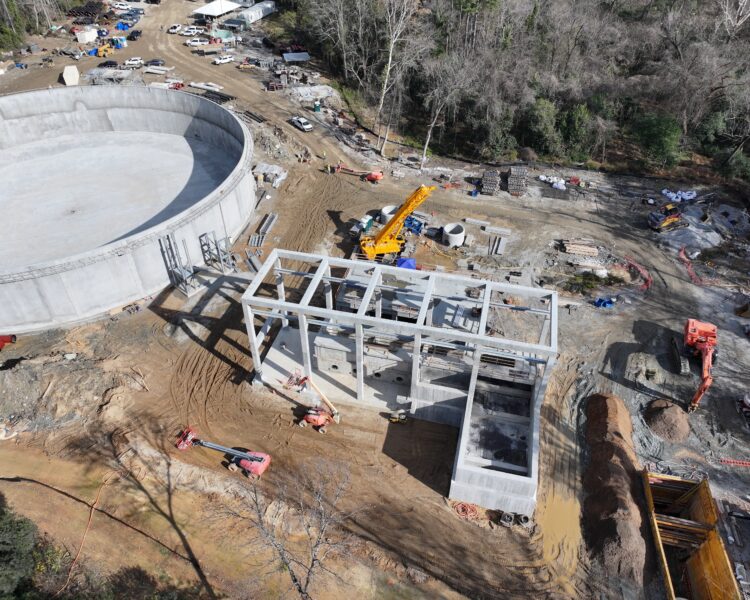 Aerial view of a circular structure, cranes, vehicles, forest.