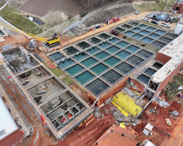 Vista aérea de una obra con depósitos, maquinaria y trabajadores.