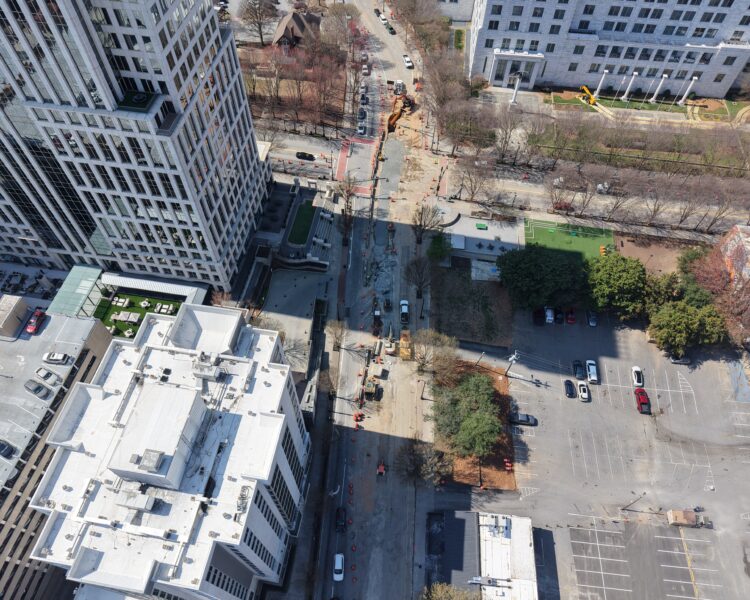 Vista aérea de las obras en una calle de la ciudad, con vehículos y conos.