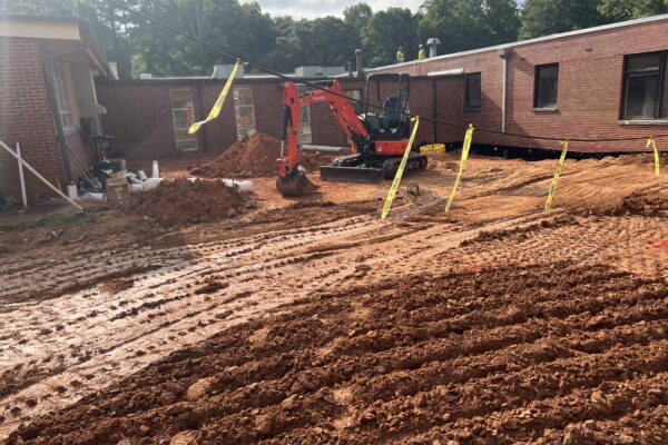 Excavadora roja excavando en una obra embarrada con cinta de precaución.