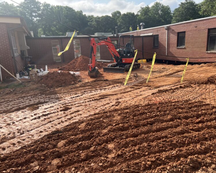 Red excavator digging at muddy construction site with caution tape.
