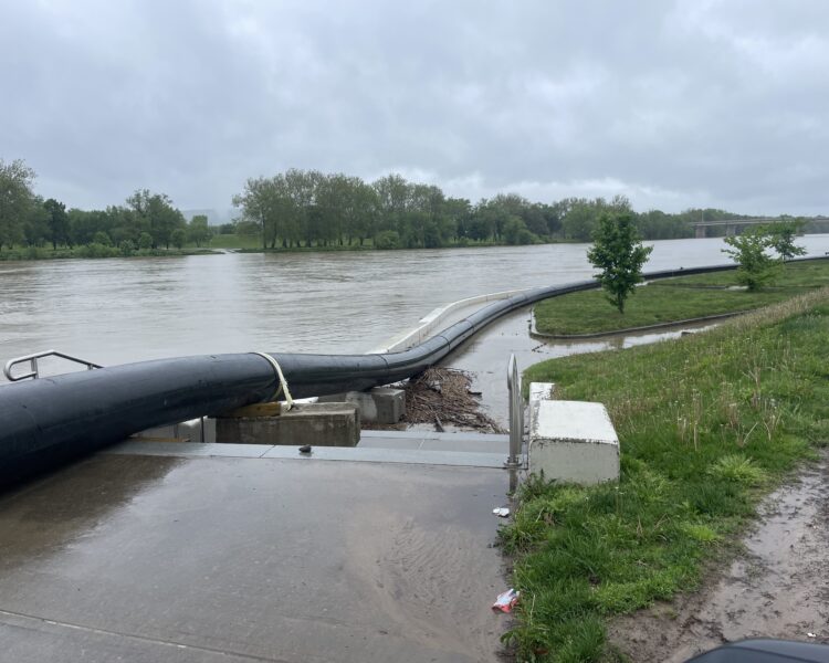 Una tubería negra conduce el agua por encima de la barrera contra inundaciones a lo largo del paseo fluvial.