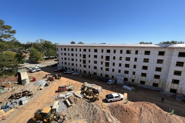 Edificio de varias plantas en construcción, con obreros y vehículos en el exterior.