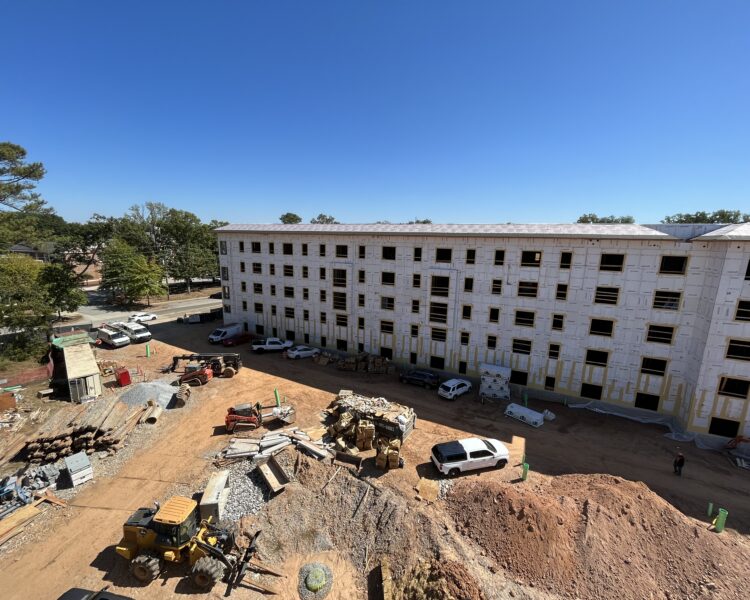Edificio de varias plantas en construcción, con obreros y vehículos en el exterior.