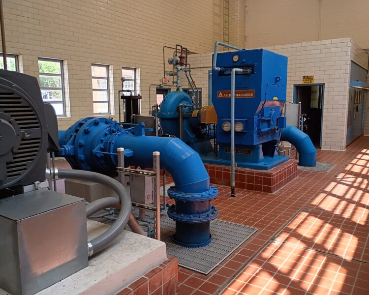 Blue pumps, pipes, and machinery in a tiled sunlit room.