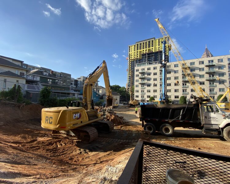 Yellow excavator, black dump truck, crane at urban construction site.
