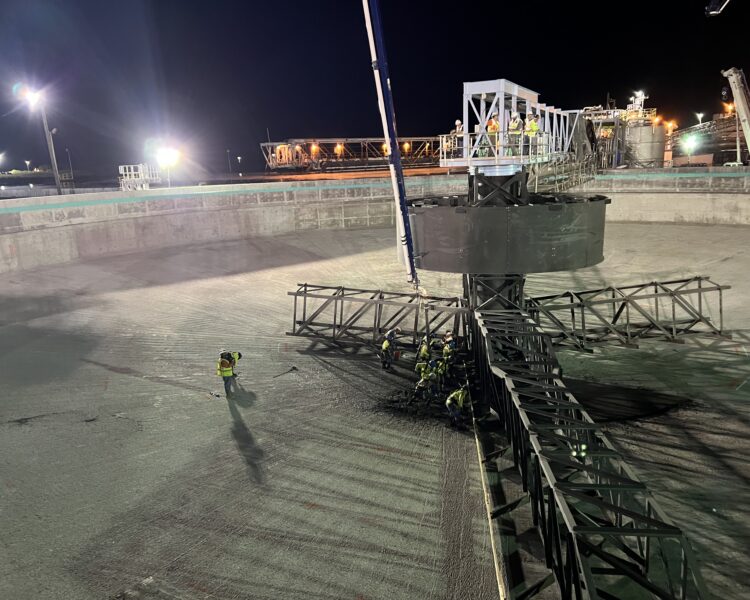 Workers in safety gear use machinery in a brightly lit, circular structure.