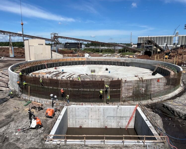 Workers assemble rebar on large circular foundation at construction site.