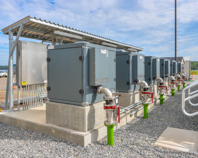 Cuadros eléctricos grises en el exterior, sobre hormigón, con tuberías.