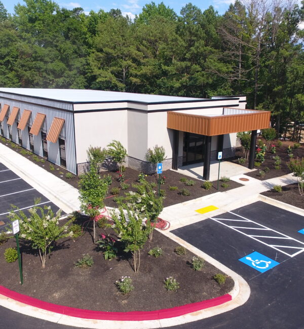 Aerial view of modern one-story building, parking, and young trees.