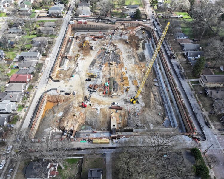 Aerial view of construction site with crane and homes nearby.