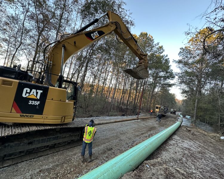 Un equipo con una excavadora CAT instala tuberías ecológicas en un sendero forestal.