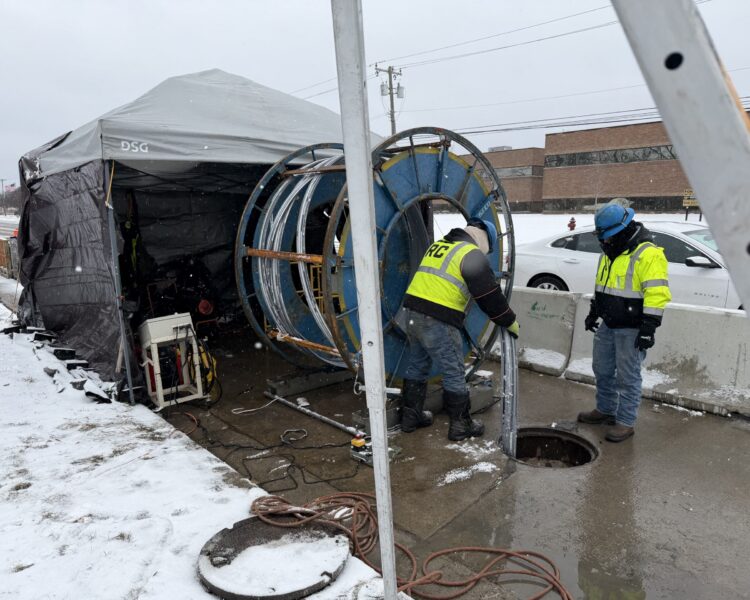Two workers in safety gear by a manhole on snowy street.