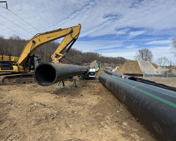 Excavator moves black pipeline on dirt construction site.
