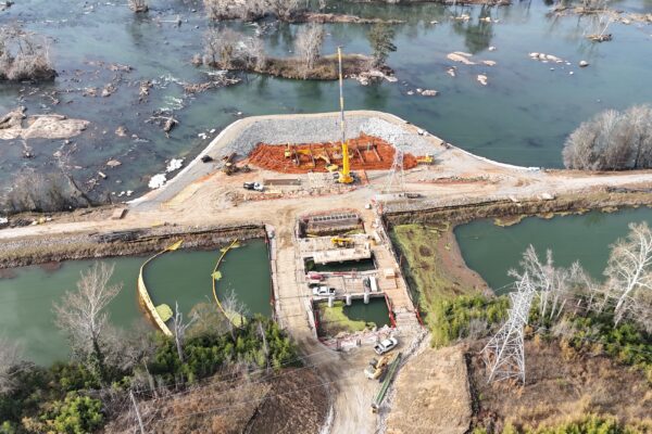 Vista aérea de grúas y vehículos construyendo una presa a orillas del río.