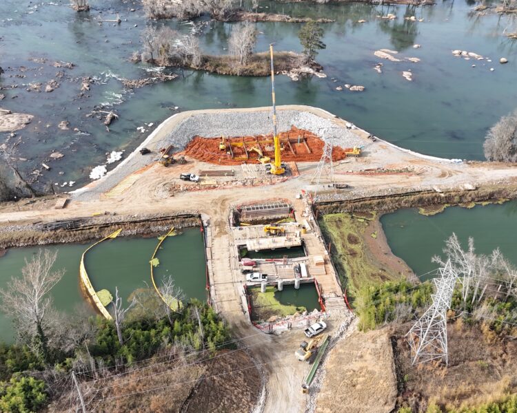 Vista aérea de grúas y vehículos construyendo una presa a orillas del río.