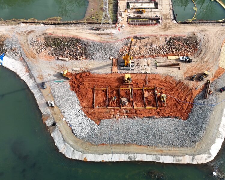 Obra en la orilla del río, rodeada de agua y maquinaria.