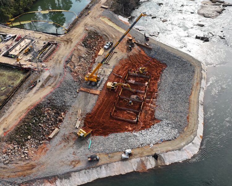 Vista aérea de una obra junto al río con grúas y maquinaria.