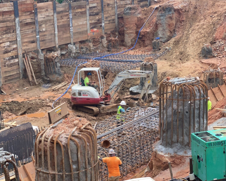 Workers, excavator, and rebar at construction site with equipment.