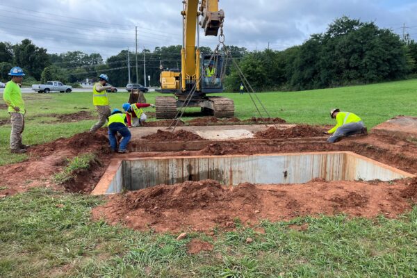 Unos trabajadores instalan una estructura de hormigón con una excavadora en un campo cubierto de hierba.