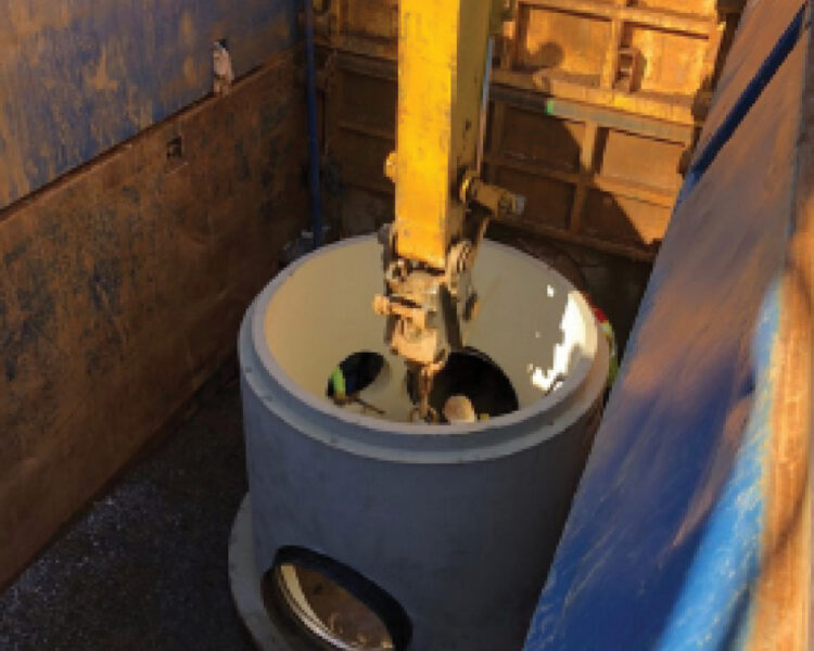 Machine lowers concrete pipe into deep excavation at work site.