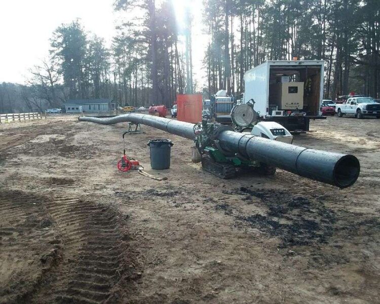 Black pipeline, welding gear, and vehicles at a forested site.