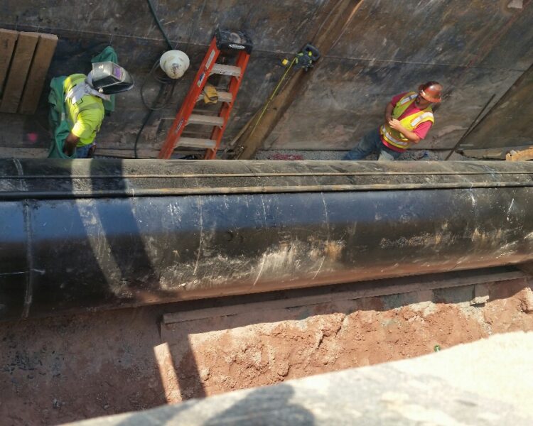 Workers in safety vests install a large black pipeline.