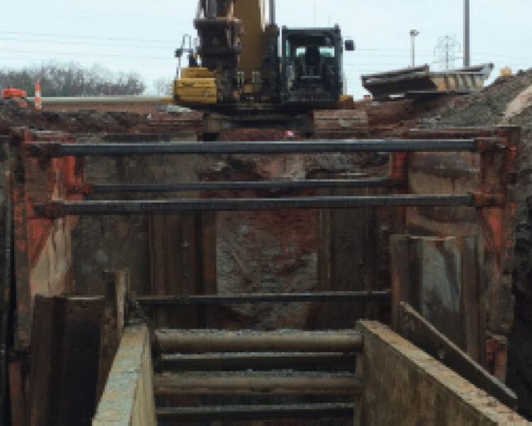 Excavator behind a deep trench with trench wall shoring.