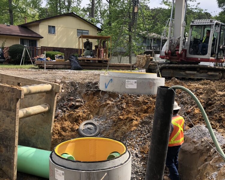 Workers use machinery to lower a concrete pipe into the ground.