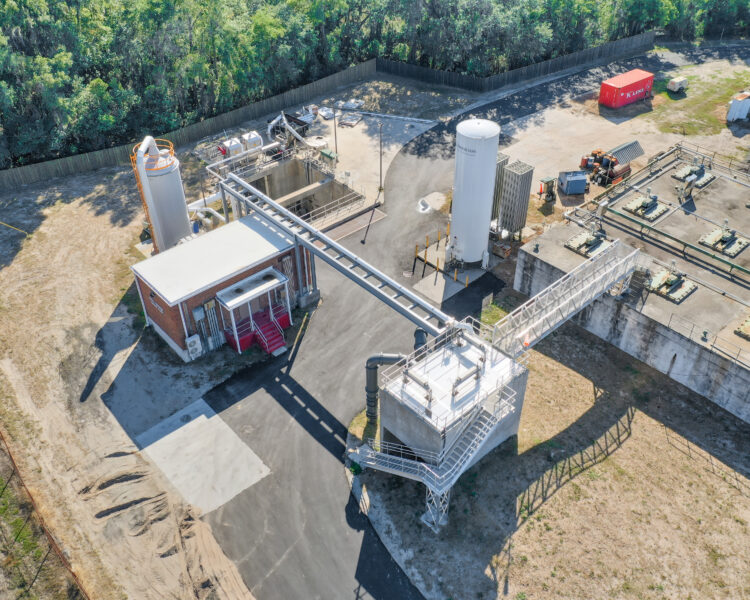 Vista aérea de un polígono industrial con depósitos, tuberías, árboles y un contenedor.