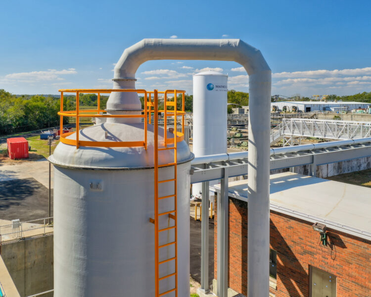 Instalación industrial con un depósito cilíndrico, barandillas naranjas y tuberías.