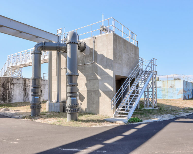 Estructura industrial de hormigón con tubos grises y escaleras metálicas en el exterior.