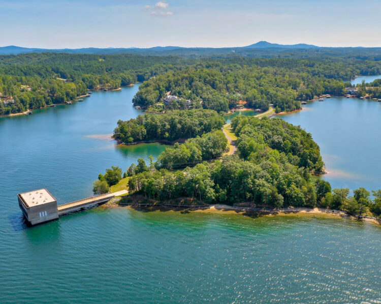 Peninsula with trees, blue lake, modern building, forested hills.